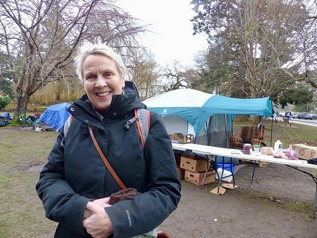 Woman in rain jacket smiling to the camera and standing in front of the community care tent in Beacon Hill Park. The tent offered donated food and drink for anyone to access in 2020.